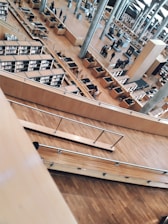 A spacious, modern library with multiple levels and rows of bookshelves. The open design features wood flooring, metallic railings, and several desks arranged for study. People can be seen walking around and engaging in activities in the background.