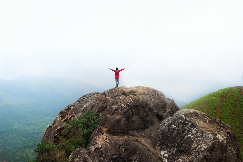 person in red long sleeve shirt standing on brown rock formation during daytime