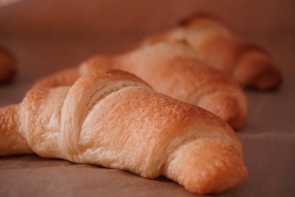 A row of freshly baked croissants with flaky layers on a blue cloth.