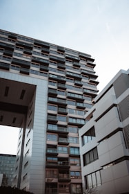 A perspective view of modern, multi-story buildings with a combination of glass and metal exteriors. The architecture features numerous rectangular windows and a large, overhanging structure creating a sense of urban development.