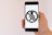 A hand is holding a smartphone displaying a banned pedestrian symbol in black on a white background. The symbol consists of a person walking, crossed out within a circle, typically used to indicate a prohibition.