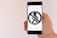 A hand is holding a smartphone displaying a banned pedestrian symbol in black on a white background. The symbol consists of a person walking, crossed out within a circle, typically used to indicate a prohibition.