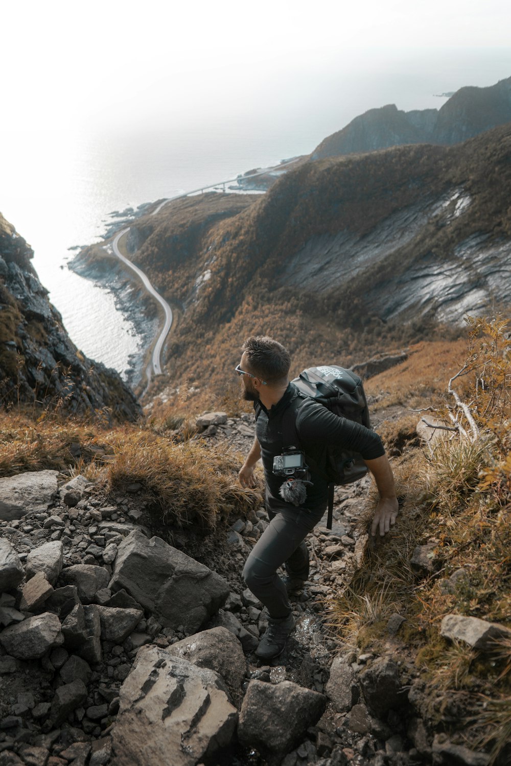 uomo in giacca nera e pantaloni neri seduto sulla montagna rocciosa durante il giorno