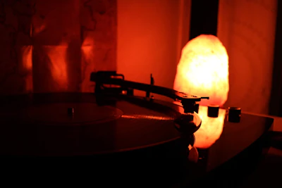 A cozy scene of a person listening to music with headphones in a dimly lit room filled with vinyl records and soft blue-red lighting.
