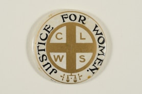 A circular pin badge with a gold cross dividing the letters 'C', 'L', 'W', 'S' in each quadrant. Surrounding the cross, the words 'Justice For Women' are printed in bold black text. The badge background is predominantly white, with a subtle decorative element at the bottom.