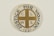 A circular pin badge with a gold cross dividing the letters 'C', 'L', 'W', 'S' in each quadrant. Surrounding the cross, the words 'Justice For Women' are printed in bold black text. The badge background is predominantly white, with a subtle decorative element at the bottom.