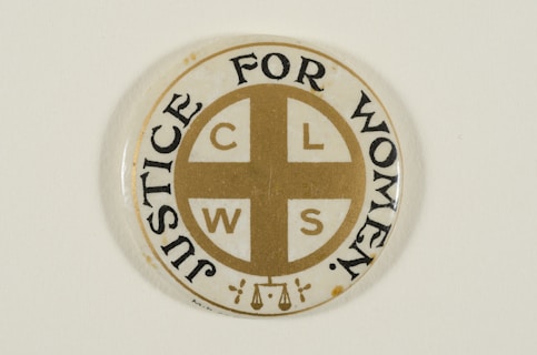 A circular pin badge with a gold cross dividing the letters 'C', 'L', 'W', 'S' in each quadrant. Surrounding the cross, the words 'Justice For Women' are printed in bold black text. The badge background is predominantly white, with a subtle decorative element at the bottom.