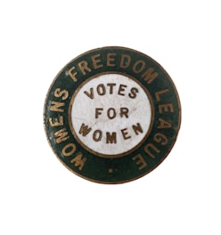 A vintage circular badge with a green outer ring and a white inner circle containing the words 'VOTES FOR WOMEN.' The outer ring features the text 'WOMENS FREEDOM LEAGUE.' The badge appears to be from a historical movement advocating for women's voting rights.