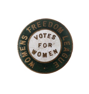 A vintage circular badge with a green outer ring and a white inner circle containing the words 'VOTES FOR WOMEN.' The outer ring features the text 'WOMENS FREEDOM LEAGUE.' The badge appears to be from a historical movement advocating for women's voting rights.