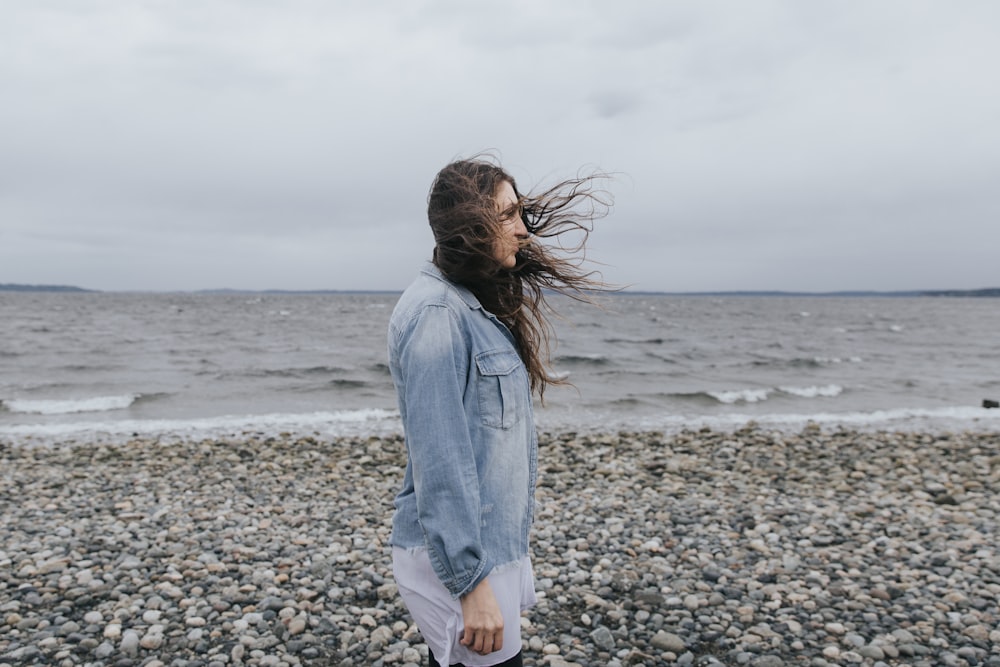 woman in blue denim jacket standing on beach shore during daytime
