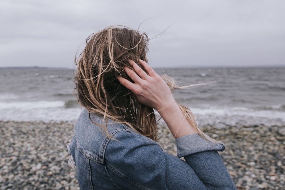 woman in blue denim jacket covering her face with her hands