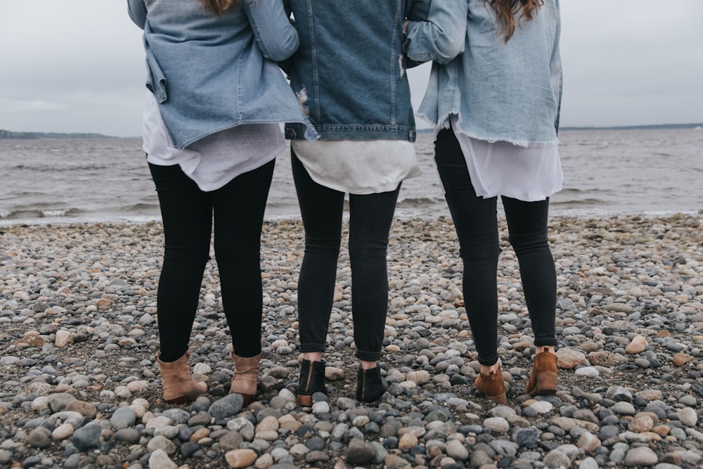 woman in blue denim jacket and black pants standing on rocky shore during daytime