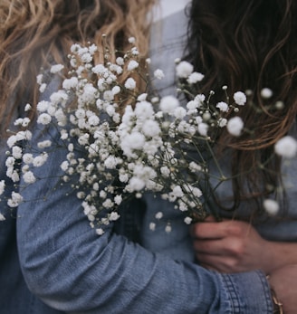 woman in gray long sleeve shirt holding white flowers