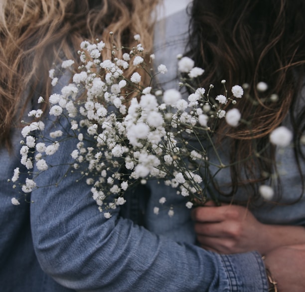 woman in gray long sleeve shirt holding white flowers