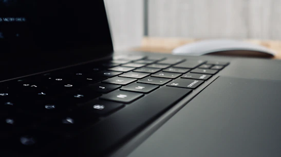 Close-up of hands typing on a sleek laptop keyboard with a dark background and subtle orange accents.