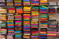 Stacks of colorful textiles from various countries spread out in a well-lit warehouse.