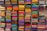 A display of colorful folded fabrics arranged neatly on shelves. The fabrics showcase a variety of patterns and textures, ranging from bright pinks, greens, and blues to intricate embroidery and designs.