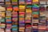 A display of colorful folded fabrics arranged neatly on shelves. The fabrics showcase a variety of patterns and textures, ranging from bright pinks, greens, and blues to intricate embroidery and designs.