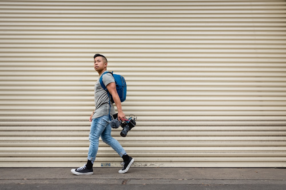 man in blue polo shirt and blue denim jeans holding black dslr camera