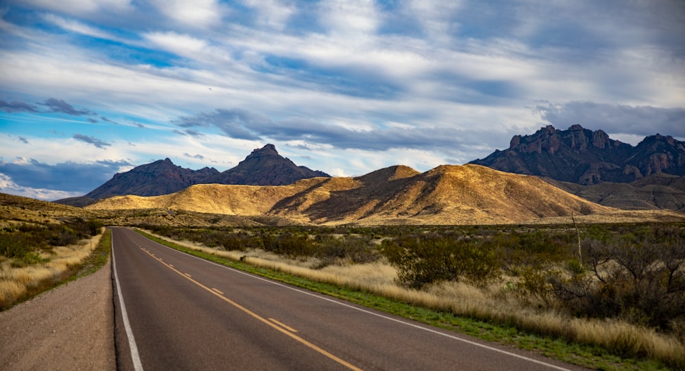 gray asphalt road near green grass field and mountains during daytime