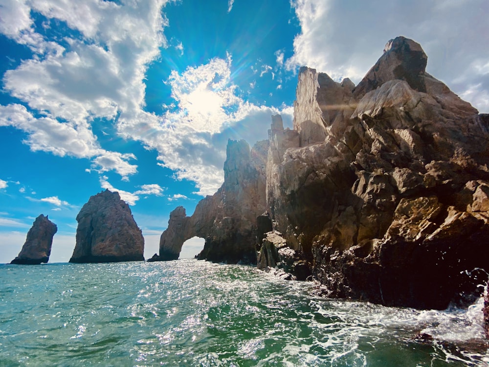 brown rock formation on sea under blue sky and white clouds during daytime