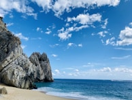 brown rock formation on sea shore under blue sky and white clouds during daytime