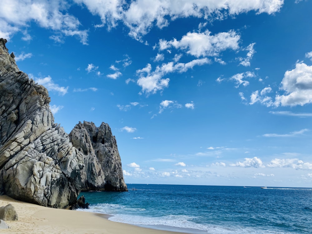 brown rock formation on sea shore under blue sky and white clouds during daytime