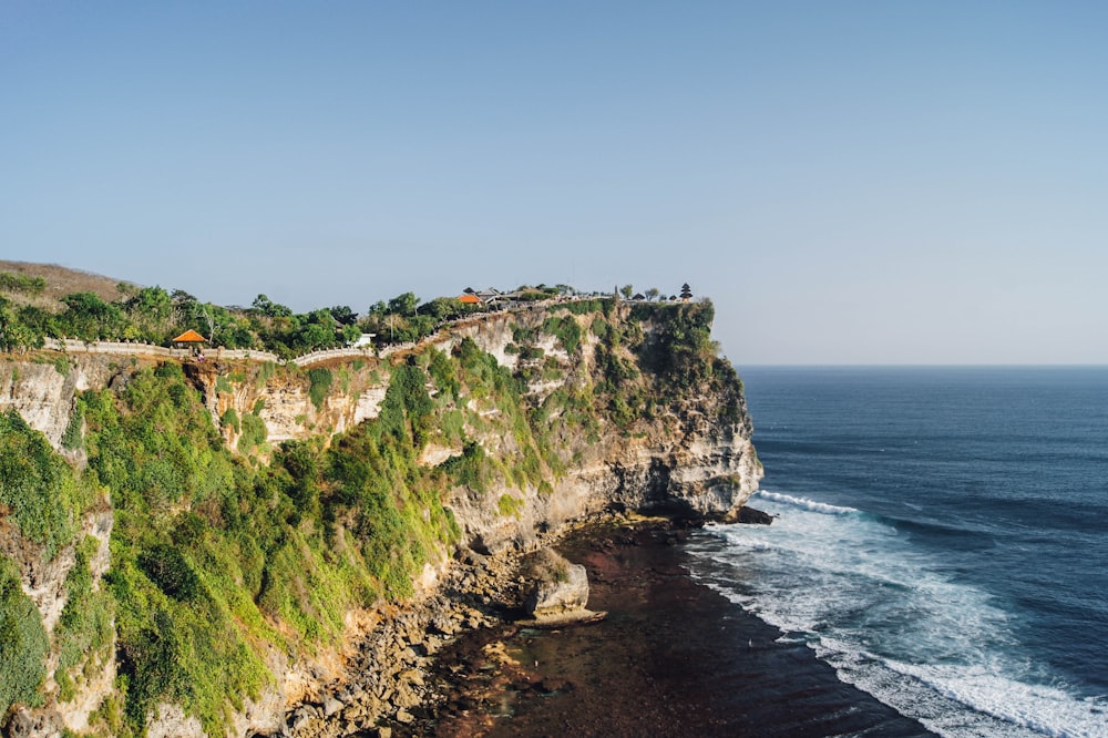 green and brown cliff beside sea under blue sky during daytime