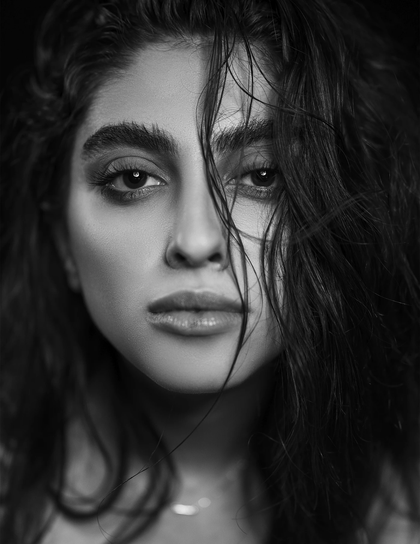 High-contrast black-and-white close portrait of a woman with prominent eyes, loose dark hair and natural-looking lips.