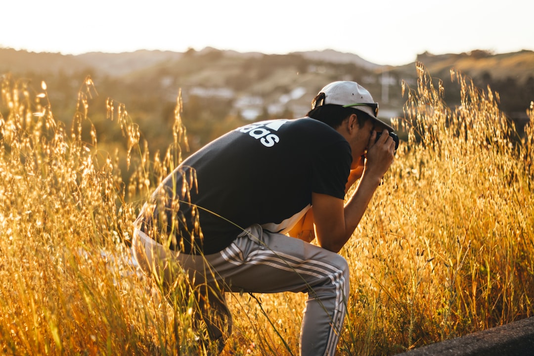 man in black t-shirt and white pants sitting on brown grass field during daytime