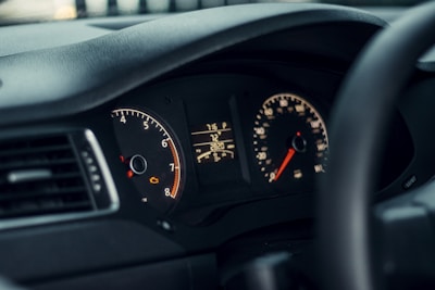 A close-up view of a car dashboard displaying the speedometer, tachometer, and various warning lights. The dashboard is illuminated with soft lighting, showcasing the vehicle's gauges and dials in detail.