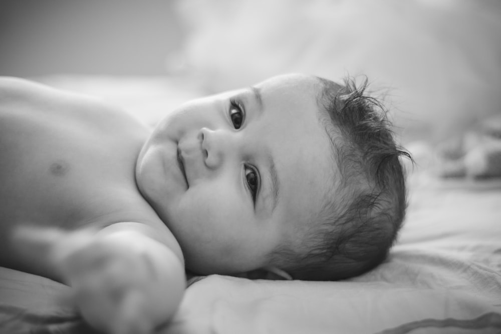 grayscale photo of baby lying on bed