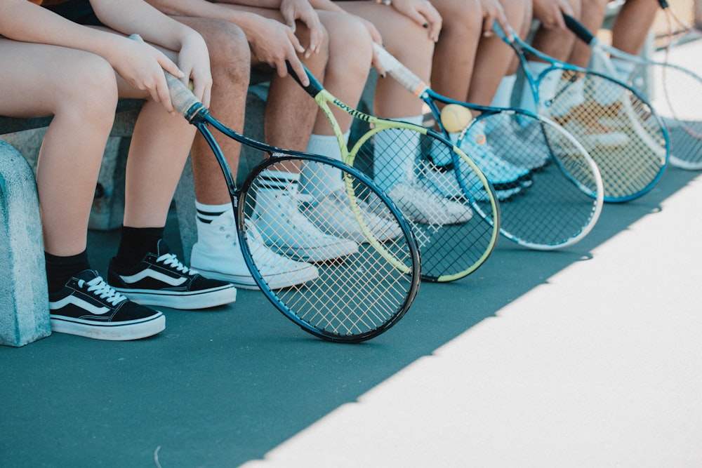 青と白のテニスラケットを持つ黒と白のナイキのスニーカーを履いた人物