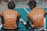 Two young people wearing orange shirts with 'YOUTH' printed on the back sit together on a sports court, viewed through a black netting. The court is blue, and one of them has a leg stretched out while they appear to be engaged in conversation or rest.