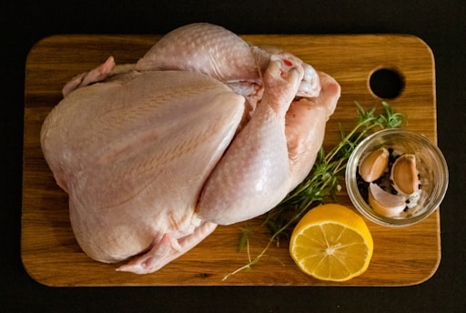 Fresh raw chicken and spices laid out on a wooden kitchen counter.
