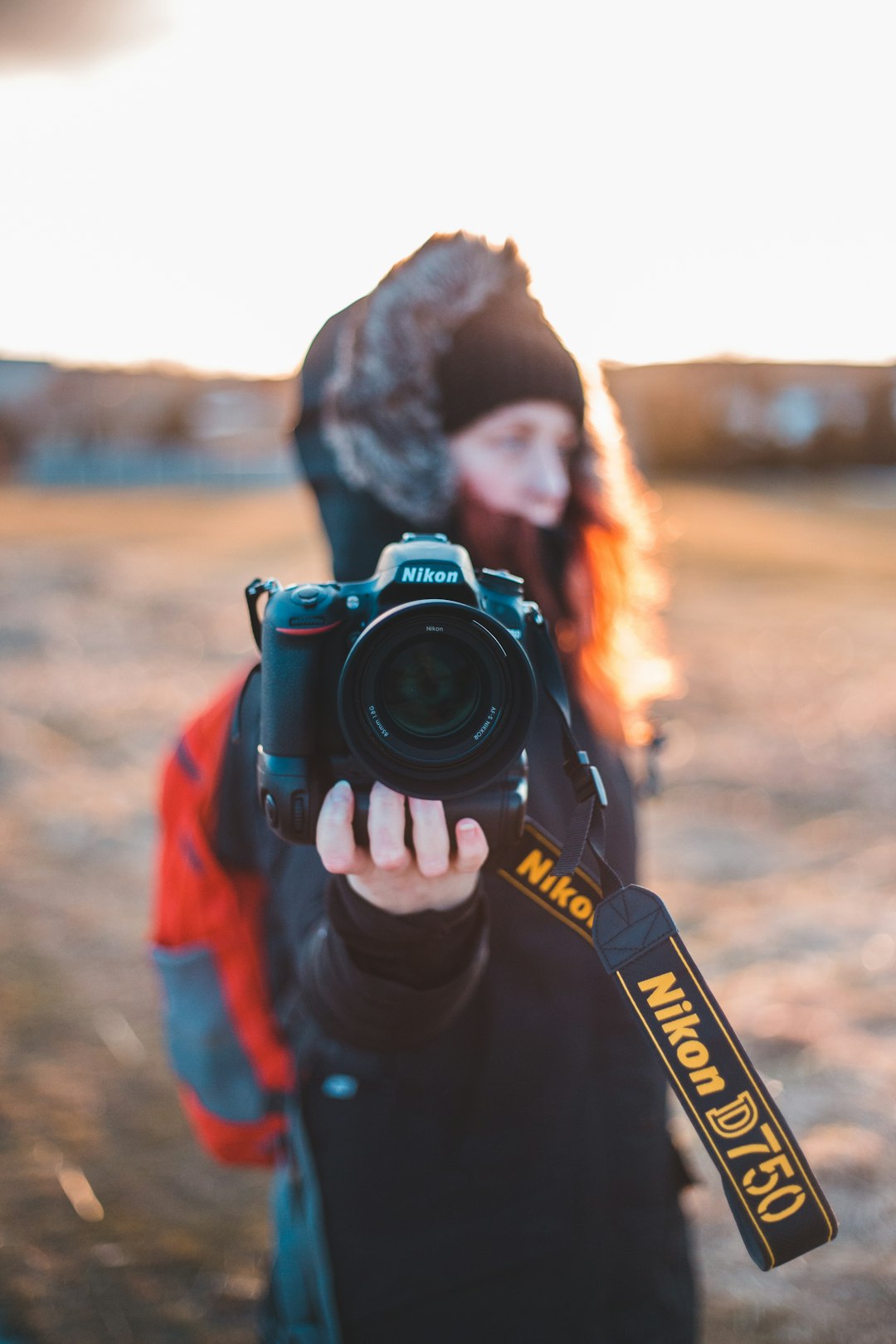 man in black and orange jacket holding black nikon dslr camera