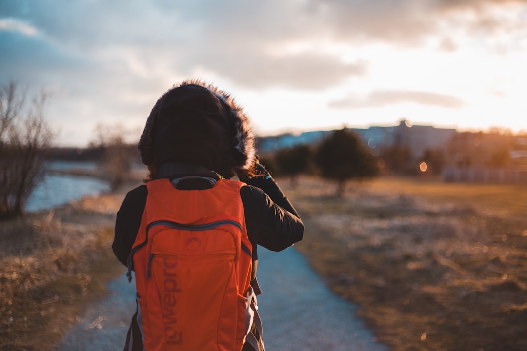 person in orange and black jacket standing on road during sunset