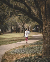 A person jogging in the park wearing lightweight headphones, surrounded by greenery.