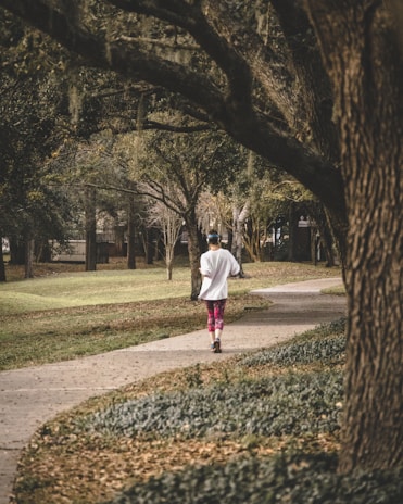 A happy woman enjoying a morning jog in a green park surrounded by trees and sunlight.