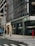 A city street scene featuring a TD Bank branch on the corner. A person is walking across a crosswalk, wearing a coat and a face mask. The building has large glass windows with the bank's logo visible. Nearby, there is a street sign indicating 'One Way' and a pedestrian crossing signal. A mailbox and other city street elements are also present.