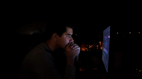 Close-up of a person’s thoughtful face illuminated by a laptop screen.