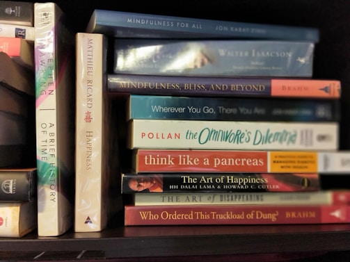 A collection of books neatly arranged on a shelf, featuring titles focused on mindfulness, happiness, and science. The spines display various colors and fonts, reflecting a diverse selection of subjects and authors.