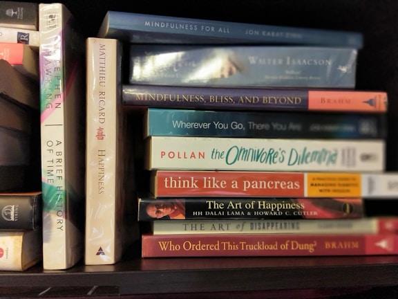 A collection of books neatly arranged on a shelf, featuring titles focused on mindfulness, happiness, and science. The spines display various colors and fonts, reflecting a diverse selection of subjects and authors.