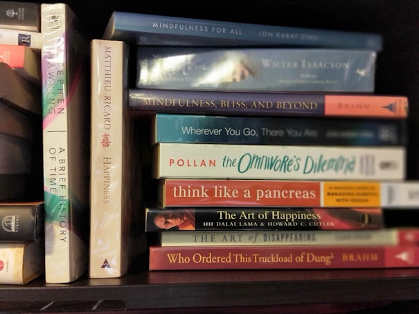 A collection of books neatly arranged on a shelf, featuring titles focused on mindfulness, happiness, and science. The spines display various colors and fonts, reflecting a diverse selection of subjects and authors.