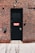 A black door with a red and white 'FACP' sign is set into a brick wall. The wall features a combination of brown and red bricks with contrasting white mortar. Above the door are two security cameras, and near the door handle, there is a small caution sign.