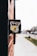 A close-up view of a black mailbox affixed to a red brick wall. The mailbox features a colorful emblem featuring mountains, a yellow road, and a pickaxe. The background is slightly blurred, showing a sidewalk and street with some greenery and indistinct buildings.