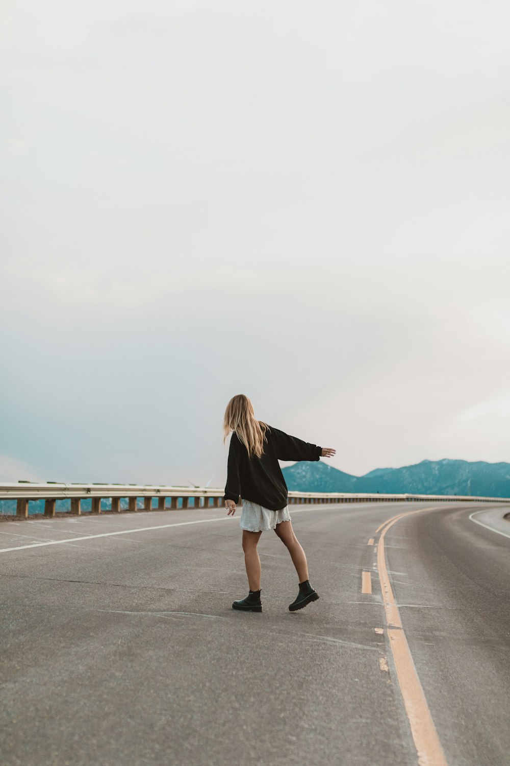 woman in black long sleeve shirt and white skirt standing on gray concrete road during daytime