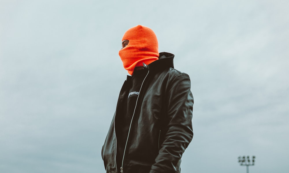 黒い革のジャケットとオレンジ色のニット帽をかぶった男