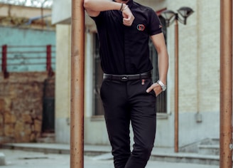 man in black polo shirt and black pants wearing black sunglasses standing on sidewalk during daytime