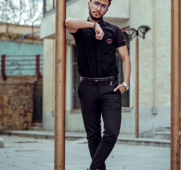 man in black polo shirt and black pants wearing black sunglasses standing on sidewalk during daytime